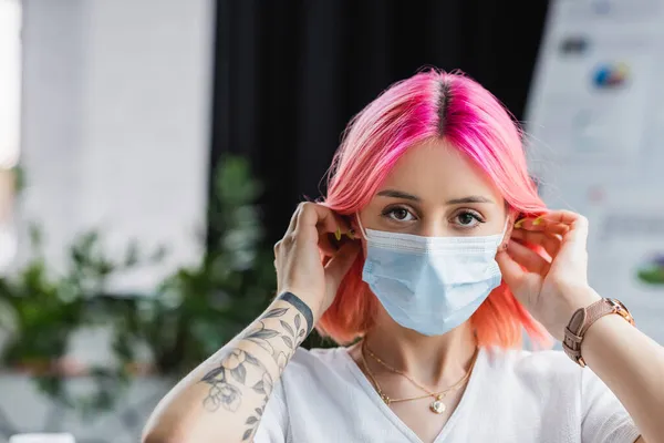 Tattooed young manager with pink hair wearing medical mask in office — Stock Photo