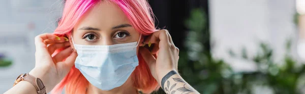 Jeune manager tatoué avec des cheveux roses portant un masque médical au bureau, bannière — Photo de stock