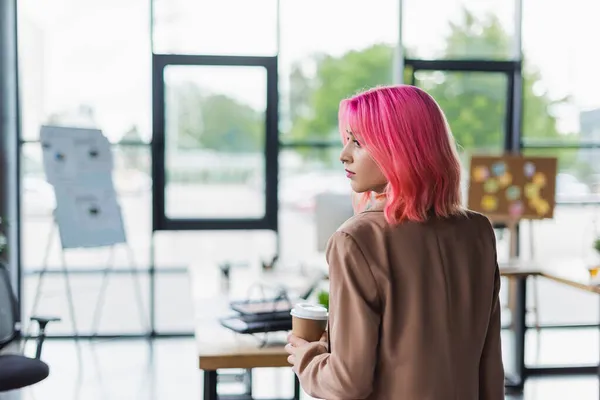 Jovem gerente com cabelo rosa e piercing segurando copo de papel no escritório — Fotografia de Stock