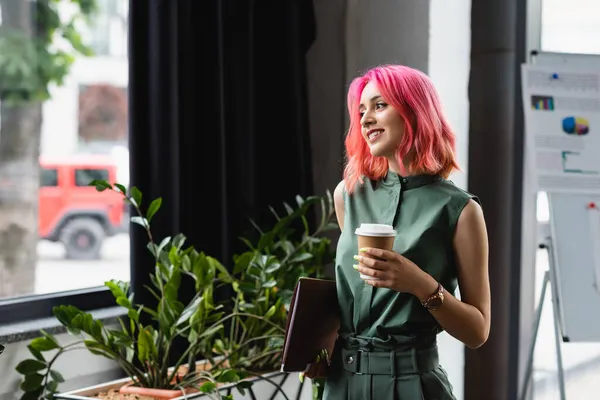 Glücklicher Manager mit pinkfarbenen Haaren und Piercing, der Pappbecher und Ordner hält — Stockfoto