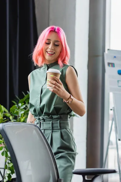 Fröhlicher Manager mit pinkfarbenen Haaren und durchdringendem Pappbecher beim Anblick des Bürostuhls — Stockfoto
