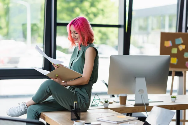 Весела бізнес-леді з рожевим волоссям і пірсингом тримає папку і документи в офісі — стокове фото