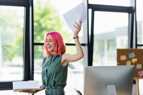 Alegre mujer de negocios con el pelo rosa y piercing carpeta de celebración con documentos en la oficina - foto de stock