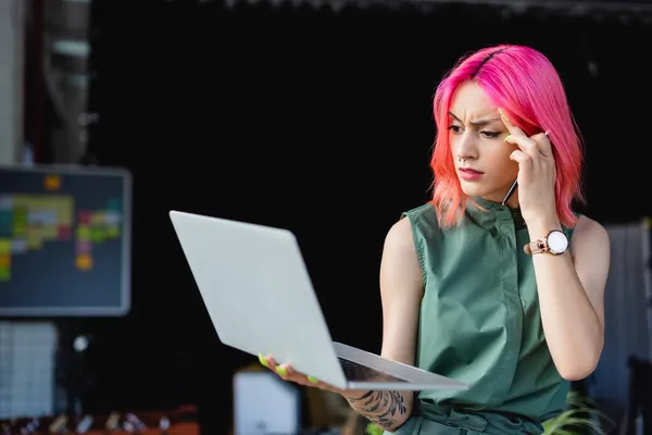 Fokussierte Geschäftsfrau mit rosa Haaren hält Stift in der Hand und blickt auf Laptop — Stockfoto