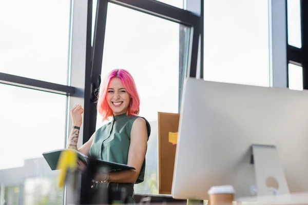 Femme d'affaires joyeuse avec dossier de tenue de cheveux roses et regardant l'écran d'ordinateur — Photo de stock