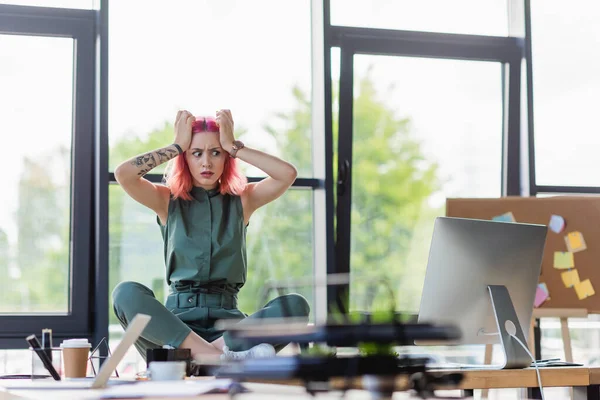 Mujer de negocios estresada con el pelo rosa sentado con las piernas cruzadas en el escritorio en la oficina - foto de stock