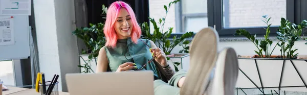 Felice donna d'affari con i capelli rosa che tiene gli occhiali mentre guarda il computer portatile, banner — Foto stock