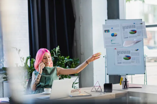 Alegre mujer de negocios con el pelo rosa hablando en el teléfono inteligente mientras lanza avión de papel - foto de stock