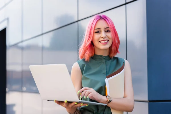 Татуювання і задоволена ділова жінка з рожевим волоссям тримає ноутбук і папку на вулиці — стокове фото