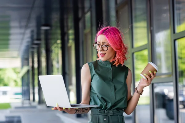 Mujer de negocios disgustado con el pelo rosa tener videollamada mientras se utiliza el ordenador portátil fuera - foto de stock