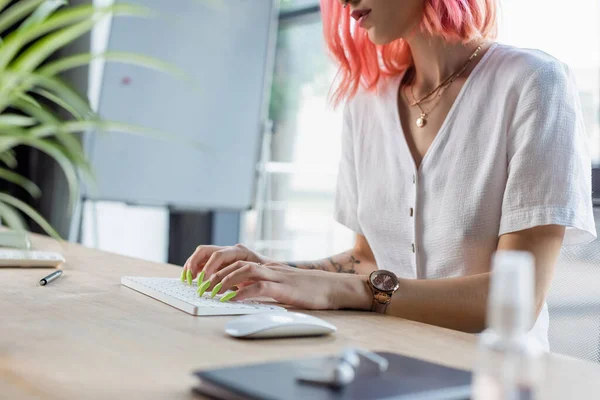 Vista recortada de la mujer de negocios perforada con el pelo rosa escribiendo en el teclado de la computadora - foto de stock