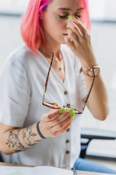 Mulher de negócios borrada e cansada com cabelo rosa segurando óculos — Fotografia de Stock