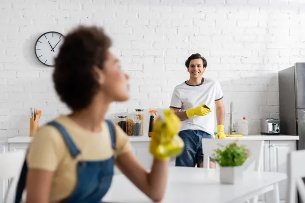 Glücklicher Mann mit Schwamm und Blick auf verschwommene afrikanisch-amerikanische Frau — Stockfoto