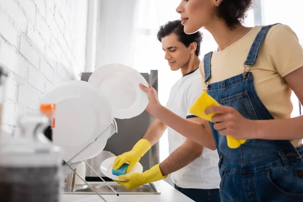 Curly african american woman holding plate and rag near blurred boyfriend — Stock Photo