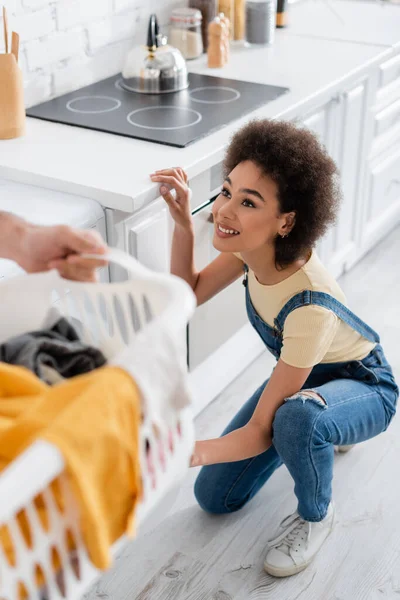 Glückliche afrikanisch-amerikanische Frau schaut Mann an, der Korb mit schmutziger Wäsche hält — Stockfoto