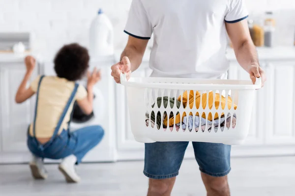 Vista recortada de hombre sosteniendo cesta con ropa sucia cerca de mujer afroamericana - foto de stock