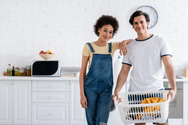Happy interracial couple near basket with dirty laundry — Stock Photo