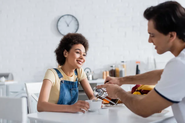 Happy african american woman looking at boyfriend pouring tea in cup — Stock Photo