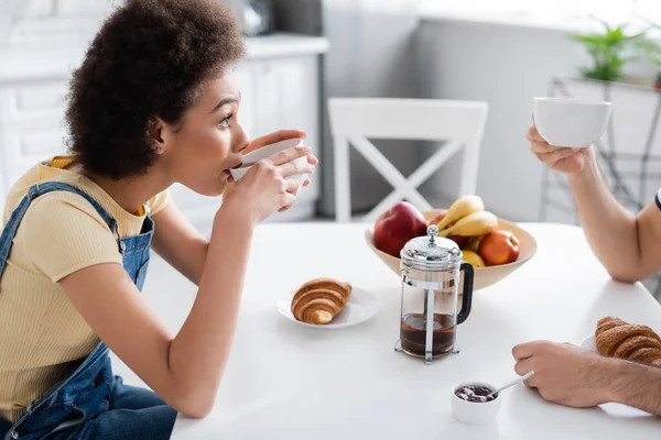 Lockige Afroamerikanerin, die Tee trinkt und ihren Freund ansieht — Stockfoto