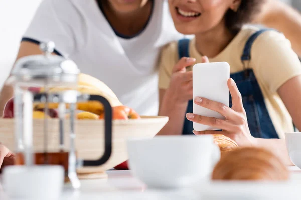 Abgeschnittene Ansicht eines glücklichen gemischtrassigen Paares mit Smartphone während des Frühstücks — Stockfoto