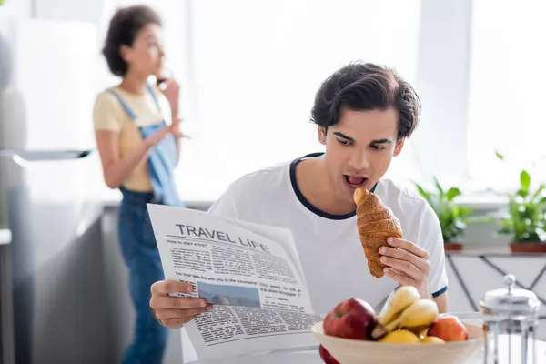 Молодой человек ест круассан и читает газету 