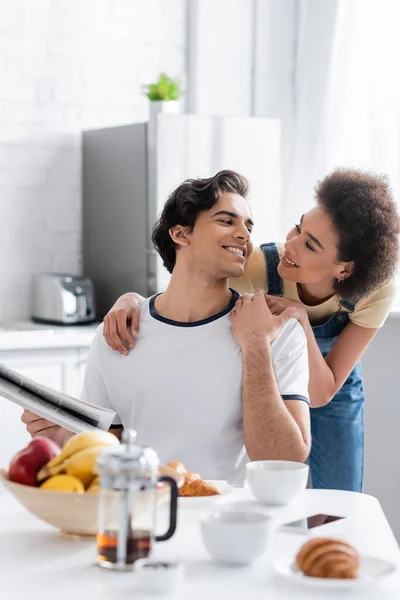 Glücklich afrikanisch-amerikanische Frau umarmt Freund mit Zeitung zu Hause — Stockfoto