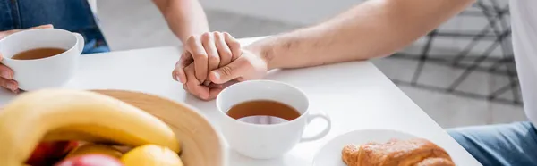Vista recortada de la pareja cogida de la mano durante el desayuno, pancarta - foto de stock