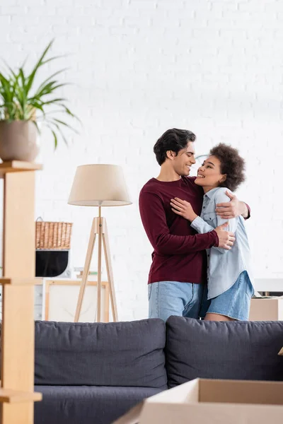 Feliz pareja multiétnica abrazando y sonriendo durante la reubicación - foto de stock