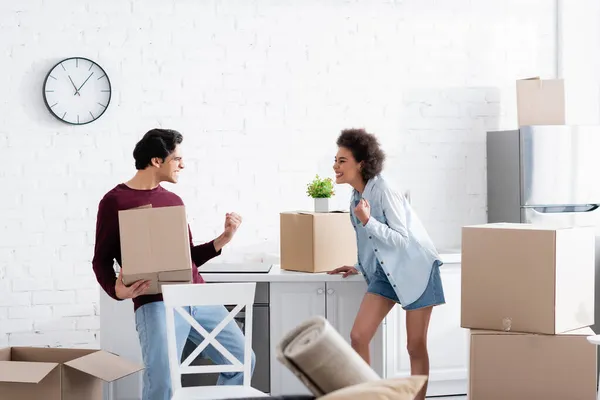 Pareja interracial emocionada celebrando la reubicación cerca de cajas de cartón - foto de stock