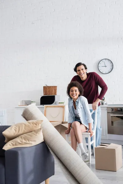 Feliz casal interracial olhando para a câmera em nova casa — Fotografia de Stock