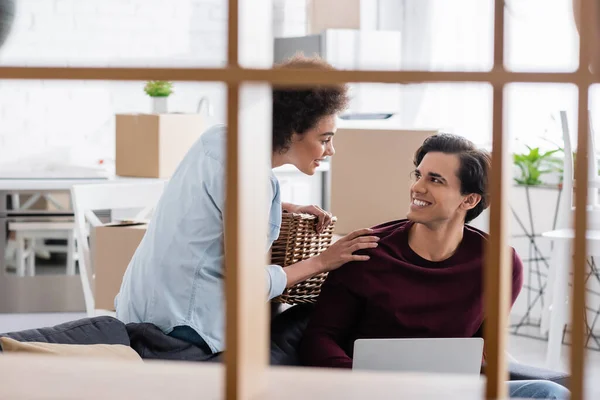 African american woman holding basket and touching shoulder of happy boyfriend with laptop — Stock Photo
