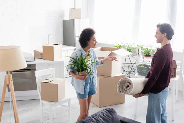 Happy african american woman with plant gesturing while talking with boyfriend during relocation — Stock Photo