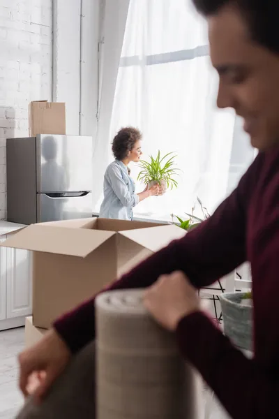 Happy african american woman with plant near blurred boyfriend on foreground — Stock Photo