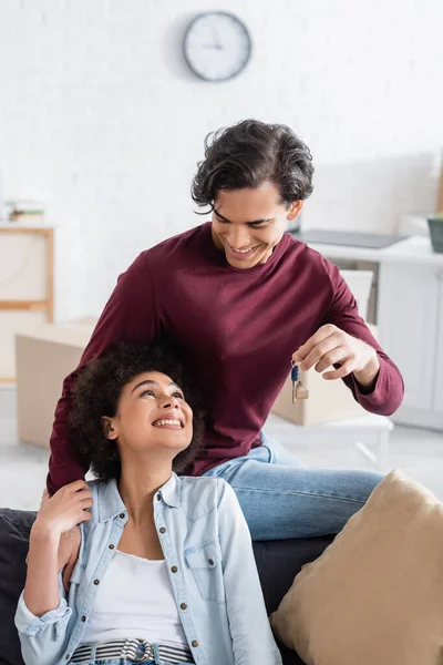Happy man holding key from new home near smiling african american girlfriend — Stock Photo