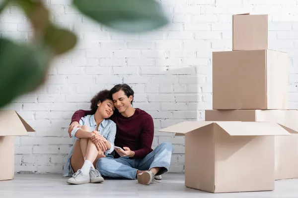 Heureux couple multiethnique assis sur le sol près de boîtes en carton — Photo de stock