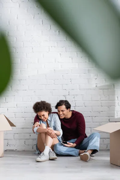 Heureux couple multiethnique assis sur le sol près de boîtes en carton — Stock Photo