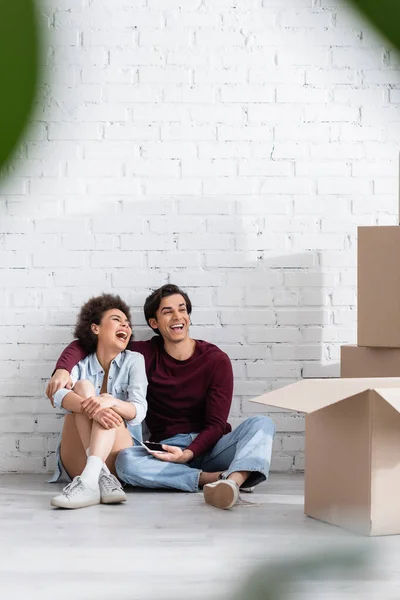 Heureux couple multiethnique assis sur le sol près de boîtes en carton — Photo de stock