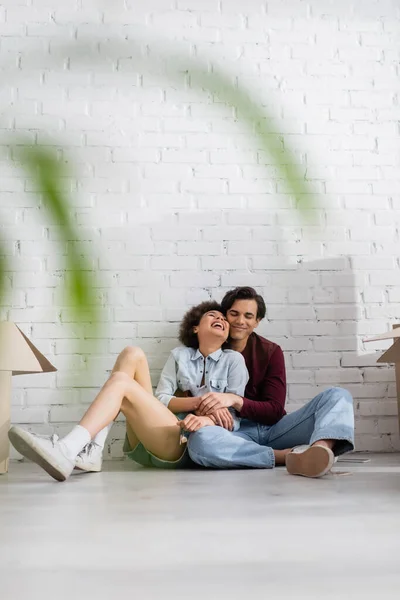 Позитивна багатоетнічна пара сидить на підлозі біля картонних коробок — стокове фото