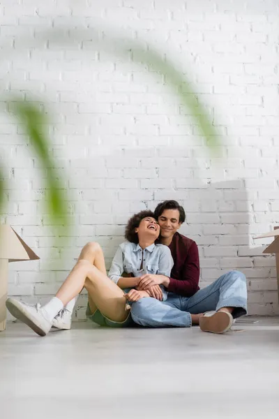 Casal multiétnico positivo sentado no chão perto de caixas de papelão — Fotografia de Stock