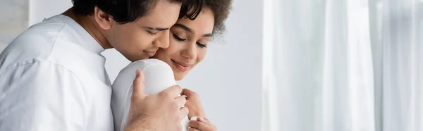 Young man hugging smiling african american girlfriend at home, banner — Stock Photo