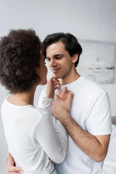 Young man smiling while looking at african american girlfriend at home — Stock Photo