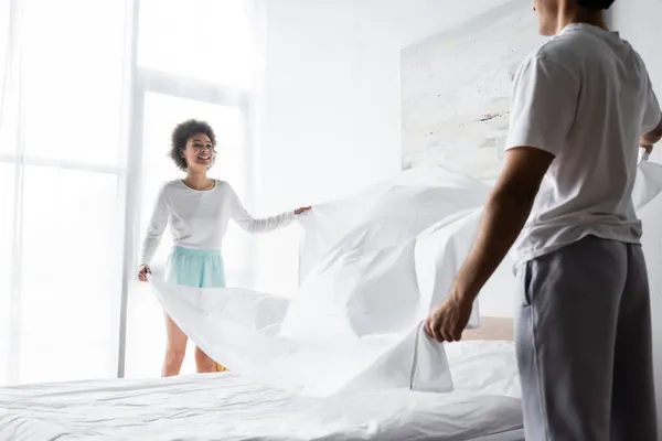 Happy african american woman arranging bed sheet with boyfriend — Stock Photo