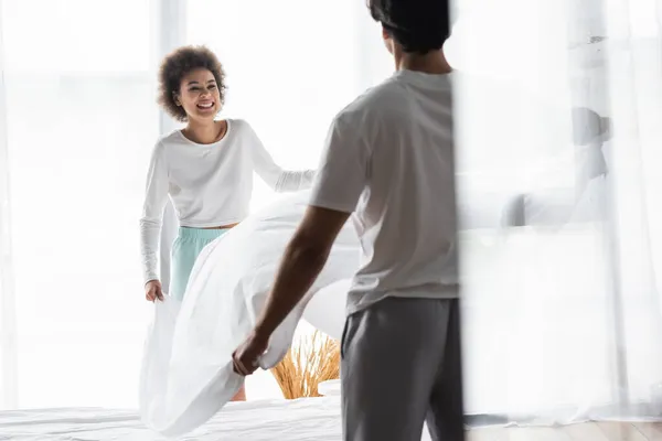 Freudige afrikanisch-amerikanische Frau arrangiert Bettlaken mit Freund — Stockfoto