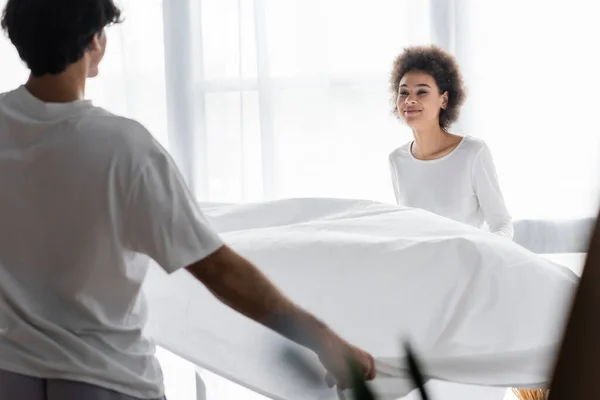 Positive african american woman arranging bed sheet with boyfriend — Stock Photo