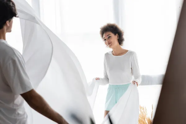 Souriant jeune femme afro-américaine organiser drap de lit avec petit ami — Photo de stock