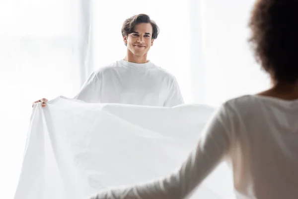 Glücklicher Mann arrangiert Bettlaken mit afrikanisch-amerikanischer Freundin — Stockfoto