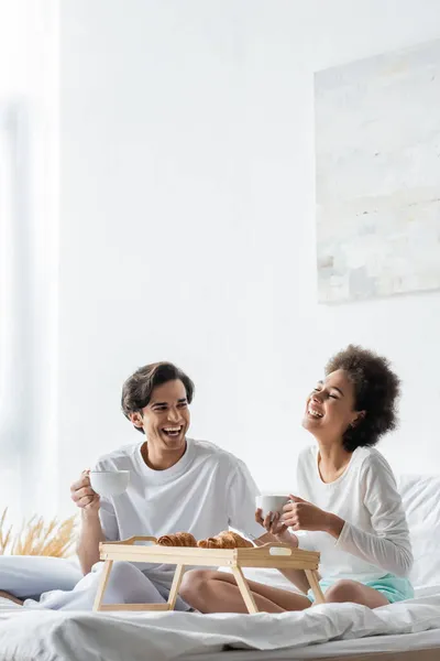 Cheerful interracial couple having breakfast in bed — Stock Photo