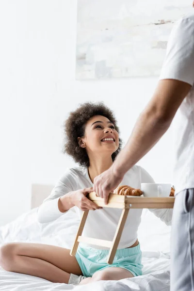 Joyful african american woman taking breakfast tray near boyfriend — Stock Photo