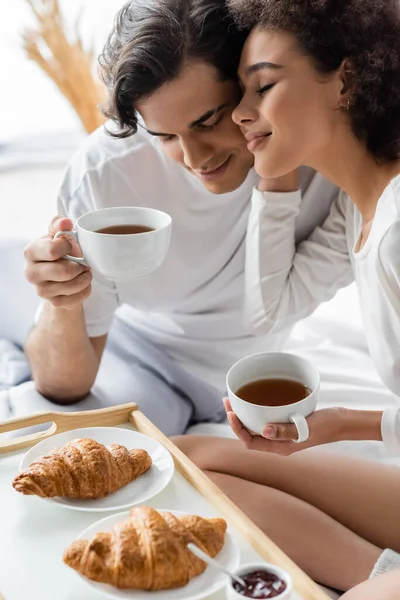 Pareja feliz e interracial desayunando en la cama - foto de stock