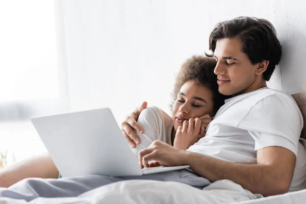 Africano americano mujer durmiendo en pecho de novio con laptop - foto de stock